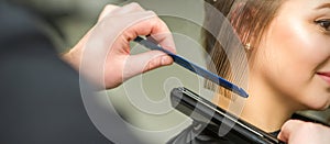 Hairstylist is straightening short hair of young brunette woman with a flat iron in a hairdresser salon, close up.