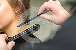 Hairstylist is straightening short hair of young brunette woman with a flat iron in a hairdresser salon, close up.