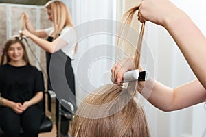 Hairstylist working on woman client with crimper photo