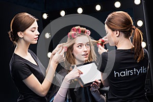 Hairstylists curling hair to woman