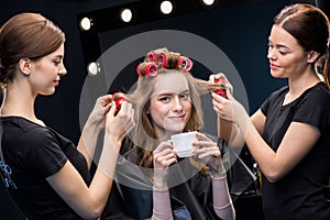 Hairstylists curling hair to woman