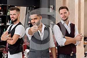 Hairstylists posing, bearded barber pointing with scissors at camera and winking.