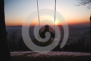 Hairy young boy aged 16-20 of European descent enjoys his life swinging on a swing at sunset on the top of Prasiva mountain in the