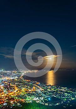 Hakodate City night view from Mt. Hakodate observatory, big bright moon light up the sea, golden reflection on surface