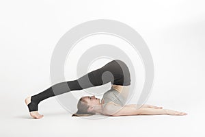 Halasana. Plow Pose. Young woman during a yoga class. Side view. Yoga trainer shows technique of performing asana on white