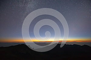 Haleakala volcano night sky with Milky Way and sunrise above the clouds