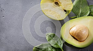 Half avocado halves with a stone, Apple, fresh green spinach leaves on a gray background, close up, copy space