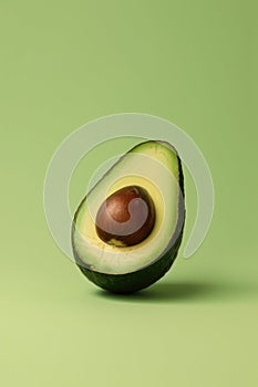 Half an avocado with pit on light green solid background