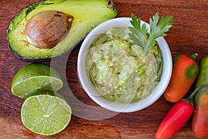 Half an avocado, some hot peppers and a lime on a wooden board and bowl with the guacamole sauce. Chopped or top view