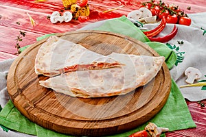 Half of the baked calzone closed type of pizza that is folded in half, on round wooden board on red wooden background
