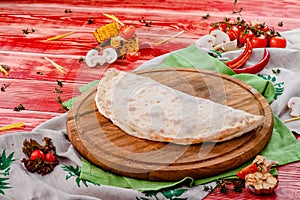 Half of the baked calzone - closed type of pizza that is folded in half, on round wooden board on red wooden background