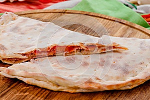 Half of the baked calzone closed type of pizza that is folded in half, on round wooden board on red wooden background