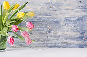 Half bouquet red and yellow tulips in green glass vase on blue shabby wooden background with copy space. Spring easter home decor.