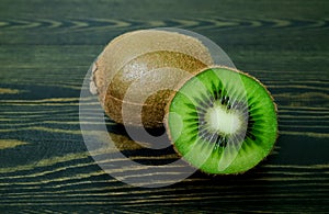 Half bright juicy ripe beautiful kiwi and whole kiwi on a coarse dark wooden background from boards