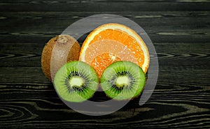 Half bright juicy ripe beautiful orange and several whole and cut kiwi halves on a coarse dark wooden background from boards