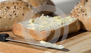 Half a Buttered Ciabatta Bread Roll with Knife.