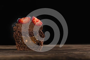 Half chocolate cupcake with filling in cut on wooden surface on black background. Fresh chocolate muffin with berries