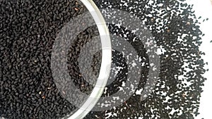 Half of circle shaped Black cumin seeds or black caraway seeds glass bowl spices spilled around it, rotating, white background