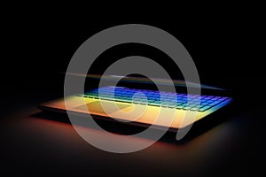 half closed laptop on dark table with colorful light reflection on keyboard