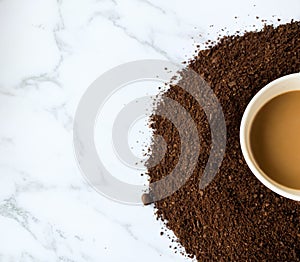 Half of coffee`s cup on roasted and ground coffee beans isolated on white marble background