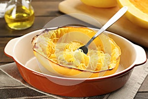 Half of cooked spaghetti squash and fork in dish on table, closeup