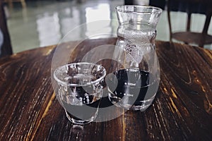 Half cup of v60 black coffee and unique beaker coffee glass jar on the wooden table