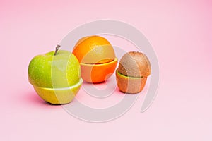 Half-cut fruits: a green apple, orange and kiwi on a pastel pink background.