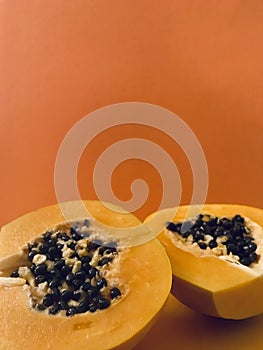 Half cut papaya on orange background. Vertical.