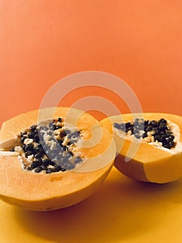 Half cut papaya on orange background. Vertical. Copy space.