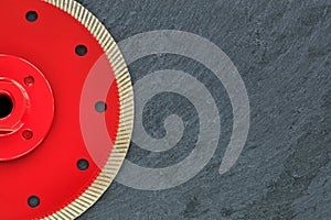 Half of the diamond cutting wheel is red with a threaded nut on a background of gray granite