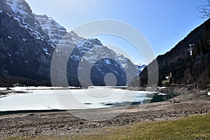 Half dried KlÃÂ¶ntalersee lake with layer of ice and panorama of Alps in background photo