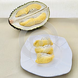 Half a durian and three durians on a white plate, on a beige background. square.