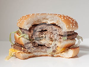 Half-eaten Burger with two cutlets on a white plate and a light background, side view