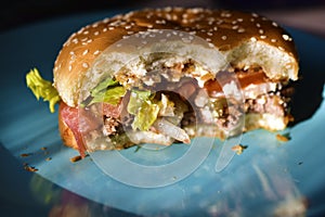 A half-eaten meat Burger with vegetables on a blue plate