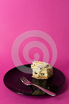 Half-eaten slice of layer cake with cream and chocolate chips on black plate, with fork