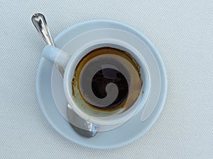 Half empty full white porcelain coffee cup, saucer and a tea spoon on white background. Top view.