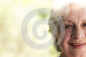 Half face of happy caucasian senior woman standing and smiling in sunny garden, copy space