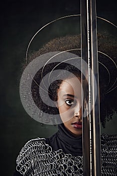 Half-face portrait of African woman with circular halos around her head and chainmail attire holding sword close face on