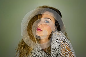 Half face portrait of a beautiful European blue eyed girl with curly dark hair on a green leaves background