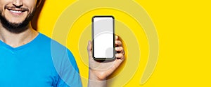 Half face portrait of man holding smartphone with mockup on yellow background with copy space.