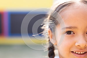 Half face portrait of smiling cauasian elementary schoolgirl in school playground, copy space photo