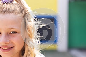 Half face portrait of smiling cauasian elementary schoolgirl in school playground, copy space photo