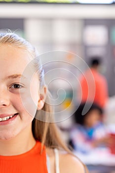Half face portrait of smiling caucasian schoolgirl in classroom, copy space photo