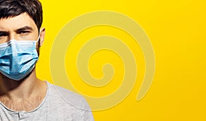 Half face portrait of young man wearing medical respiratory face mask against coronavirus on background of yellow color with copy.