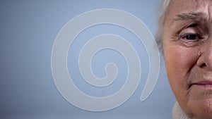 Half-face of upset crying elderly woman on grey background, poverty hopelessness