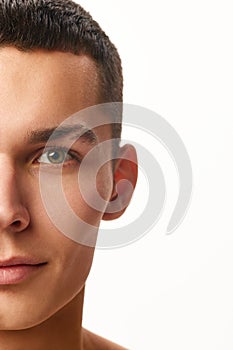 Half-faced portrait of handsome young man with shaved, spotless face with cheekbones against white studio background