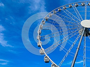 Half of the Ferris wheel is metallic in color with closed booths on a background of rich blue sky