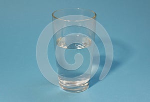 Half-filled glass of clean cold water on a light blue background. Healthy life  proper nutrition  drink plenty of water