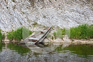 Half-flooded wooden boat on rocky shore of mountain river from sheer cliffs