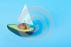 Half of fresh avocado fruit - yacht or sailboat with sail on blue background